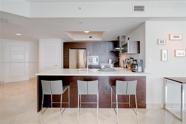 kitchen with a kitchen breakfast bar, appliances with stainless steel finishes, a tray ceiling, and light tile floors