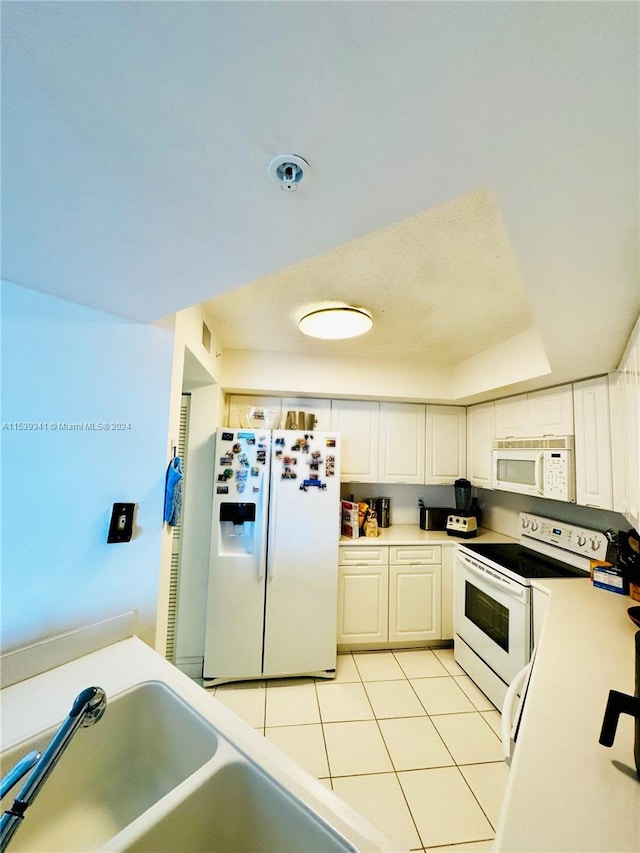 kitchen featuring white appliances, light tile flooring, white cabinetry, and sink