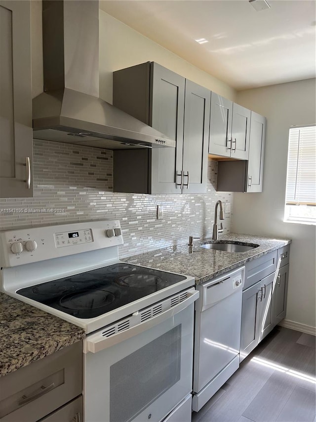 kitchen featuring white appliances, wall chimney exhaust hood, stone countertops, decorative backsplash, and sink