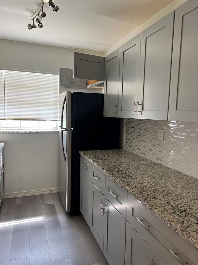 kitchen with gray cabinetry, stainless steel fridge, light stone counters, backsplash, and rail lighting