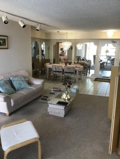 living room featuring a textured ceiling, a notable chandelier, rail lighting, and tile patterned floors