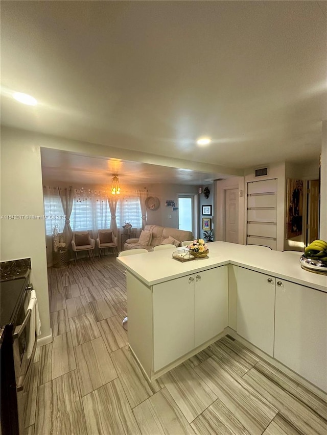 kitchen featuring a peninsula, visible vents, open floor plan, light countertops, and stainless steel electric range oven