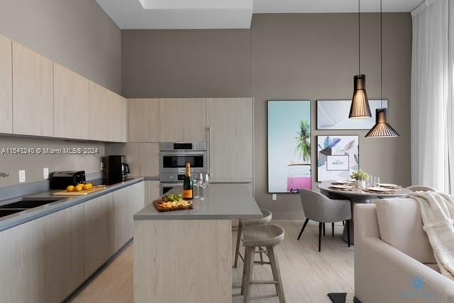 kitchen featuring a kitchen bar, light hardwood / wood-style flooring, pendant lighting, double oven, and a center island