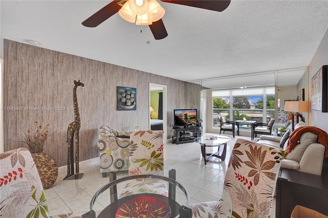 living room featuring ceiling fan, wood walls, a textured ceiling, and light tile patterned flooring