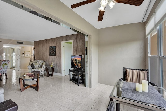 living room featuring wooden walls, light tile patterned floors, and ceiling fan