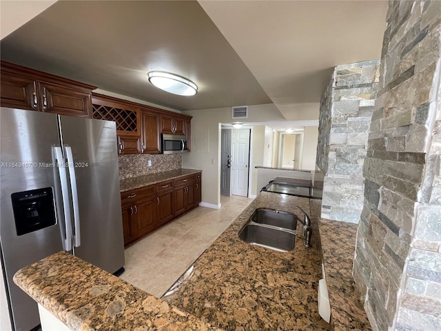 kitchen with appliances with stainless steel finishes, light tile floors, sink, tasteful backsplash, and dark stone counters