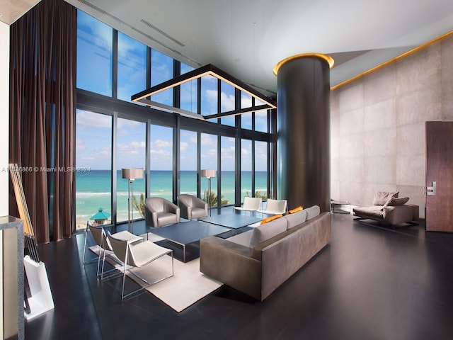 living room featuring a towering ceiling, a water view, a wall of windows, and a wealth of natural light