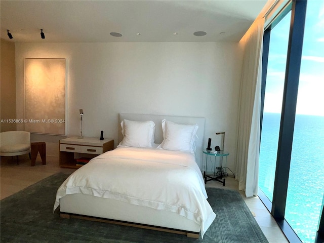 bedroom with a water view, light tile flooring, expansive windows, and access to exterior