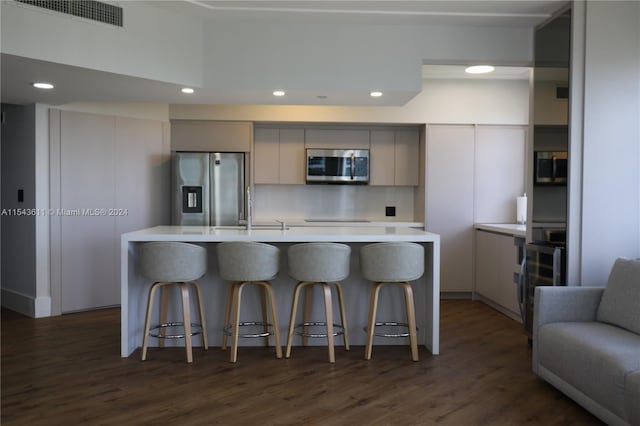 kitchen with a center island, a kitchen bar, dark wood-type flooring, appliances with stainless steel finishes, and backsplash