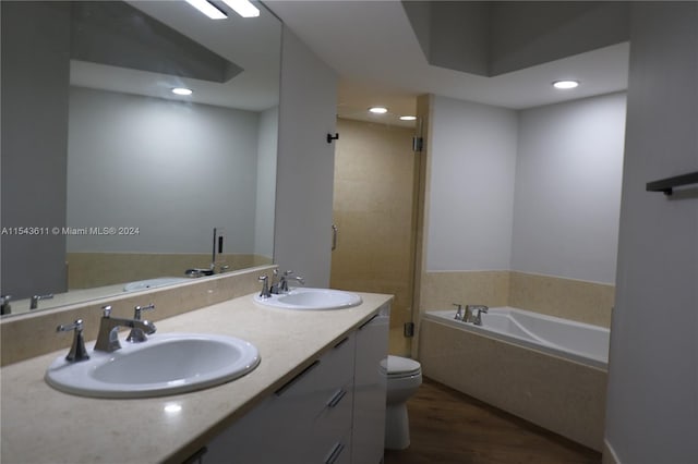 bathroom featuring toilet, large vanity, hardwood / wood-style flooring, a bath, and dual sinks