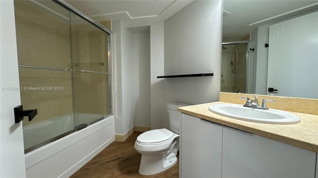 full bathroom featuring wood-type flooring, toilet, oversized vanity, and bath / shower combo with glass door