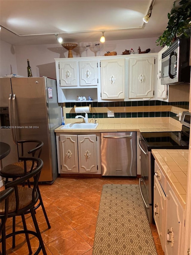 kitchen featuring tile counters, white cabinets, appliances with stainless steel finishes, backsplash, and track lighting