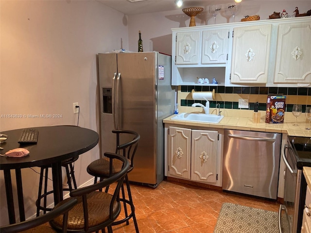 kitchen with appliances with stainless steel finishes, white cabinets, backsplash, tile countertops, and sink