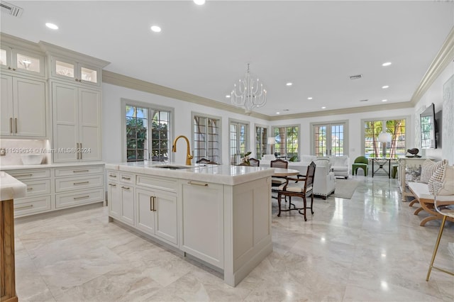 kitchen with a notable chandelier, crown molding, white cabinetry, sink, and a center island with sink