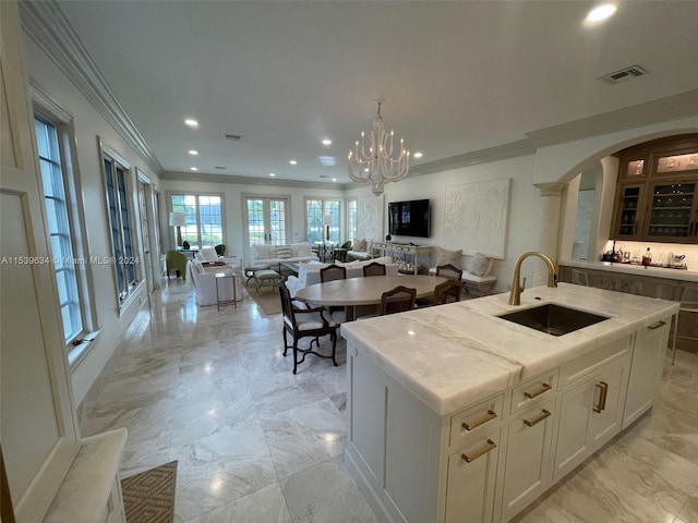 kitchen featuring crown molding, white cabinetry, a chandelier, an island with sink, and sink