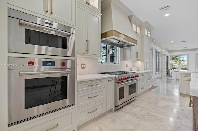 kitchen with backsplash, crown molding, custom exhaust hood, white cabinetry, and double oven range