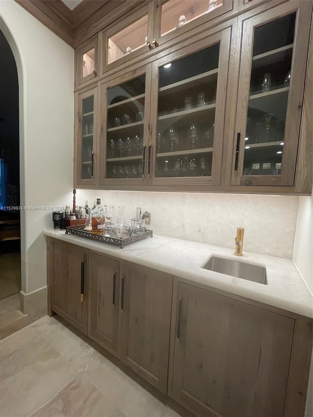 bar with backsplash, dark brown cabinetry, and sink