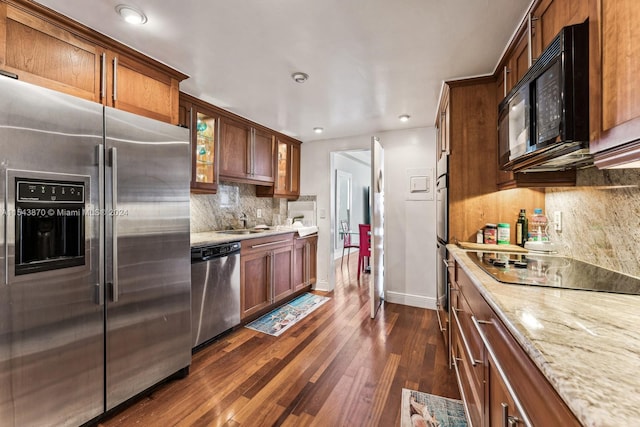 kitchen featuring light stone countertops, dark wood-type flooring, black appliances, backsplash, and sink