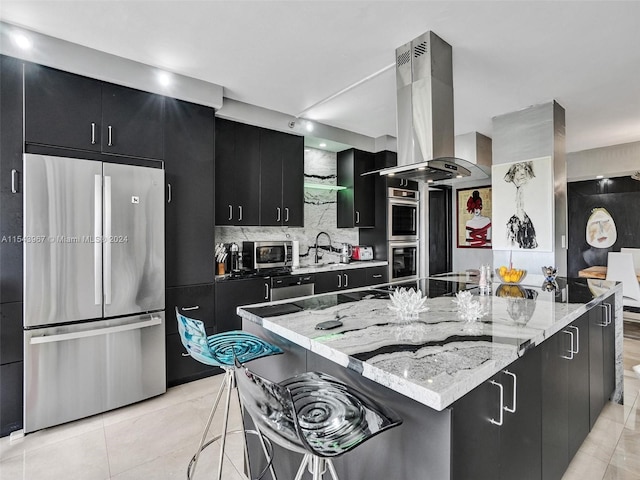 kitchen featuring stainless steel appliances, light tile flooring, a breakfast bar area, backsplash, and island exhaust hood