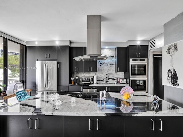 kitchen with island range hood, stainless steel appliances, light stone countertops, tasteful backsplash, and sink