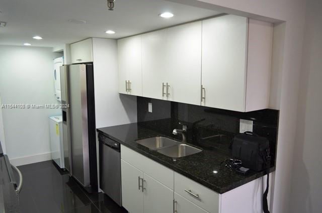 kitchen featuring stacked washer / dryer, stainless steel appliances, white cabinetry, and sink