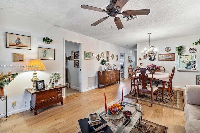 living room featuring a textured ceiling, light wood-type flooring, and ceiling fan with notable chandelier