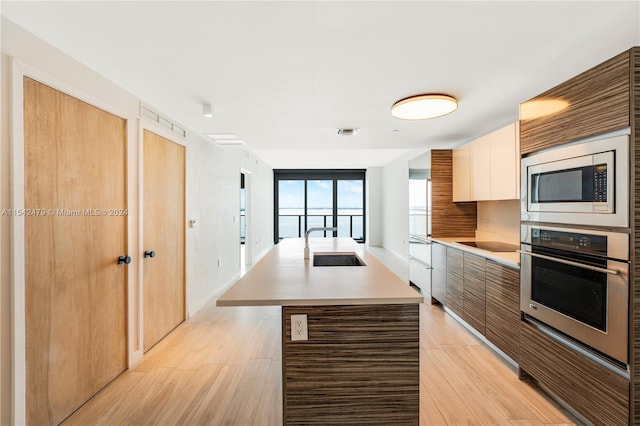 kitchen with stainless steel appliances, a center island with sink, white cabinets, sink, and light hardwood / wood-style floors