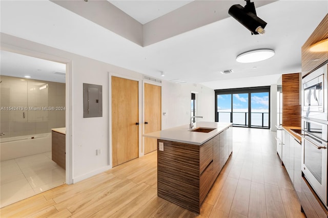 kitchen featuring sink, oven, a center island with sink, electric panel, and light tile patterned floors