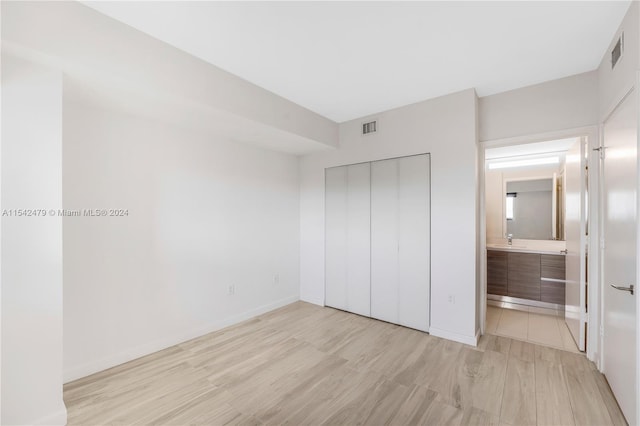 unfurnished bedroom with sink, light wood-type flooring, a closet, and connected bathroom