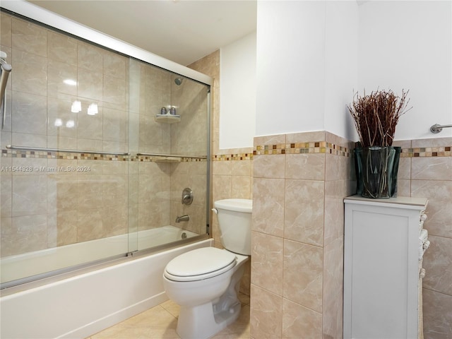 bathroom featuring tile patterned floors, toilet, shower / bath combination with glass door, and tile walls