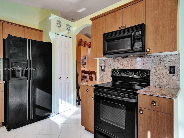 kitchen featuring black appliances, light stone countertops, light tile patterned floors, and tasteful backsplash