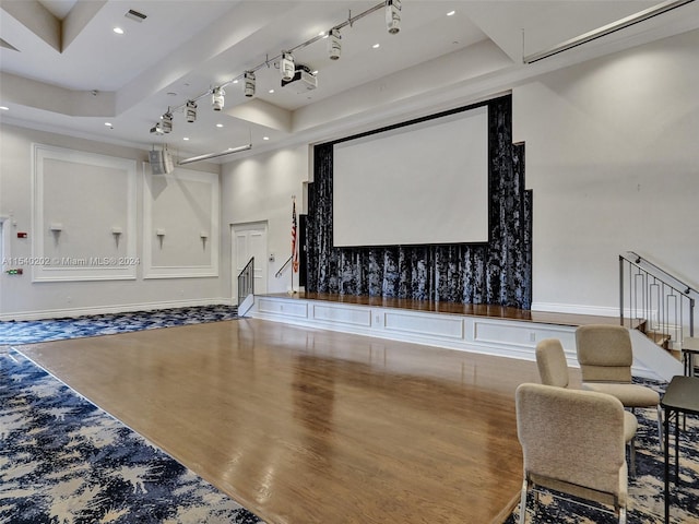 cinema featuring hardwood / wood-style flooring, a raised ceiling, a towering ceiling, and rail lighting