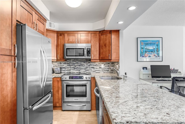 kitchen with light stone counters, sink, decorative backsplash, and stainless steel appliances