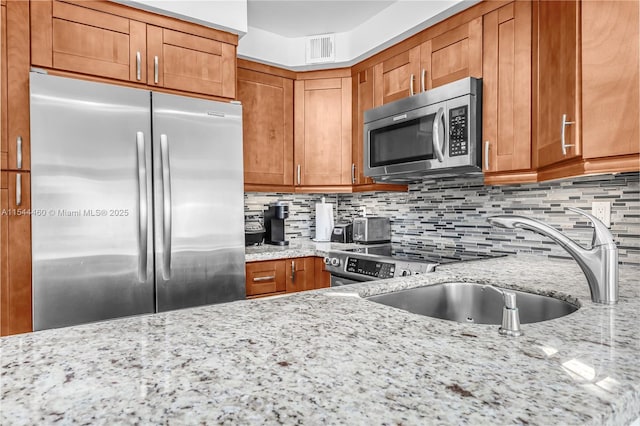 345 Ocean Dr Unit 411, Miami Beach, FL 33139 - kitchen featuring stainless steel appliances, brown cabinetry, light stone countertops, and tasteful backsplash