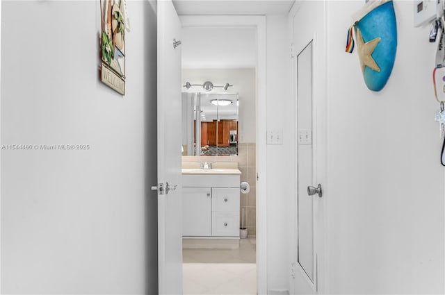 corridor with light tile patterned floors, tile walls, and sink