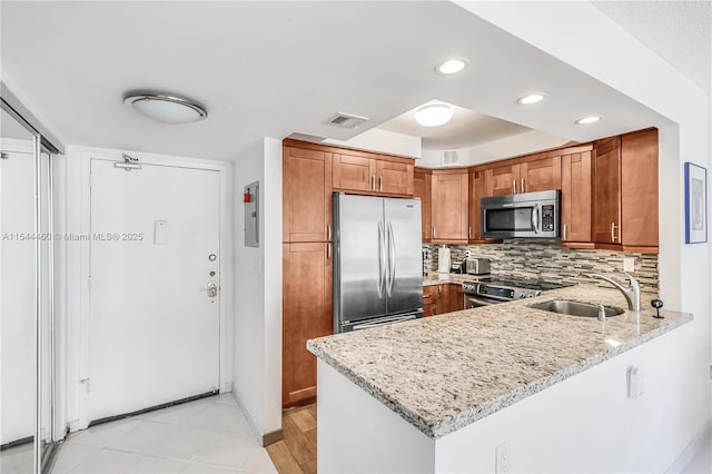 kitchen featuring backsplash, kitchen peninsula, sink, light stone countertops, and stainless steel appliances