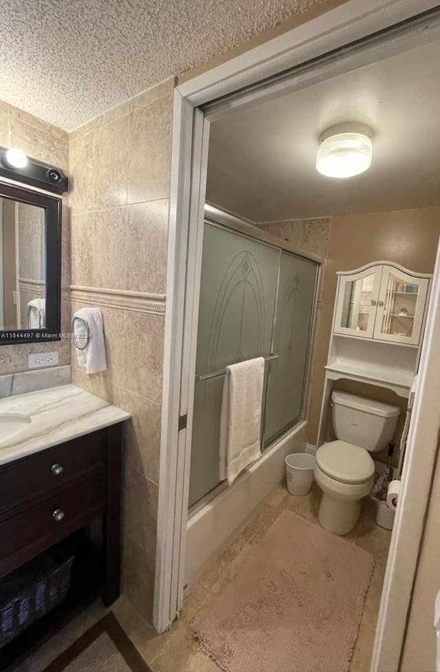 full bathroom with tile patterned flooring, vanity, tile walls, toilet, and combined bath / shower with glass door