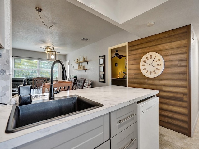 kitchen featuring sink, dishwasher, a textured ceiling, ceiling fan with notable chandelier, and white cabinetry