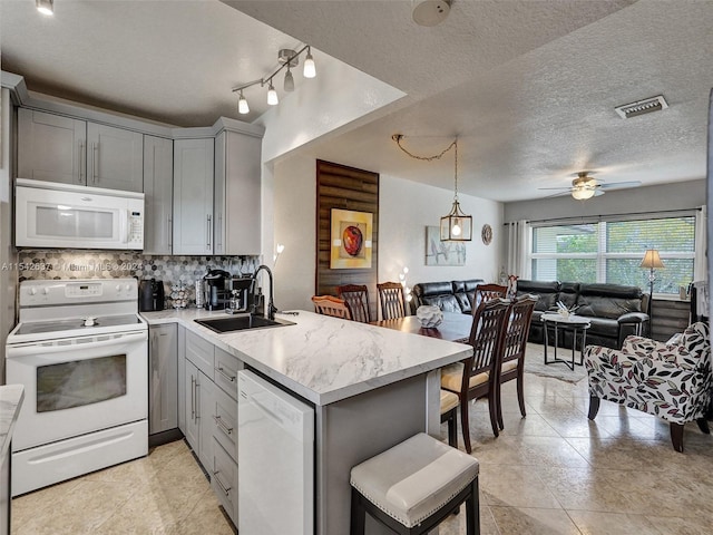 kitchen featuring a textured ceiling, ceiling fan with notable chandelier, kitchen peninsula, white appliances, and sink