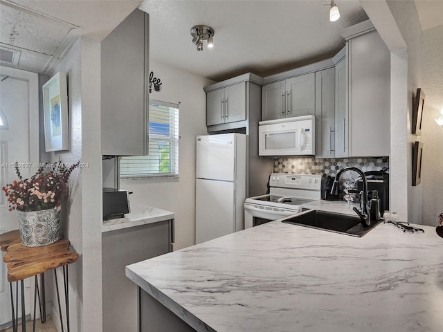 kitchen with white appliances, sink, gray cabinets, backsplash, and a kitchen bar