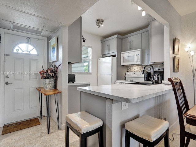 kitchen featuring light tile floors, a breakfast bar, white appliances, gray cabinetry, and backsplash