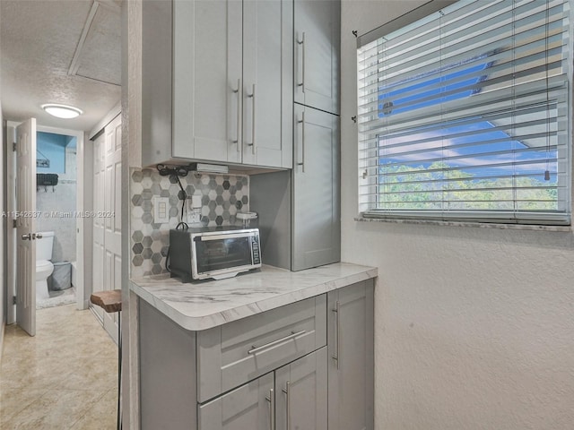 kitchen featuring backsplash, light tile floors, a textured ceiling, and gray cabinets