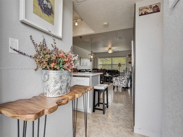 kitchen featuring white cabinets, a textured ceiling, hanging light fixtures, and a breakfast bar area