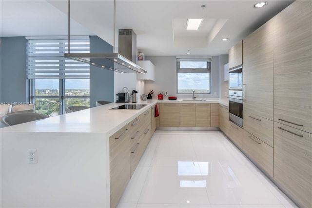 kitchen featuring wall chimney exhaust hood, a healthy amount of sunlight, sink, and light tile floors