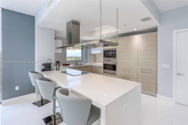 kitchen with island range hood, light tile floors, a breakfast bar, hanging light fixtures, and sink