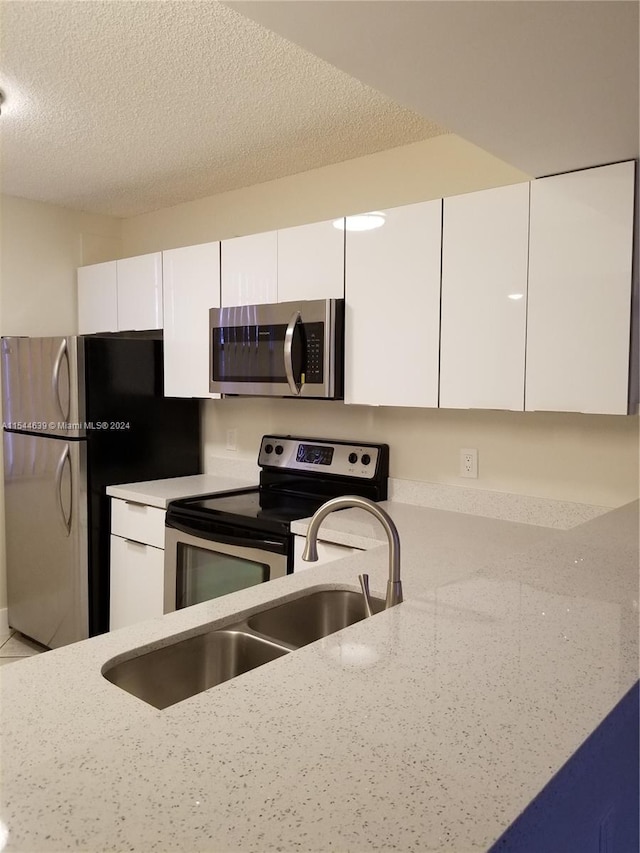 kitchen featuring white cabinetry, a textured ceiling, appliances with stainless steel finishes, and light stone counters