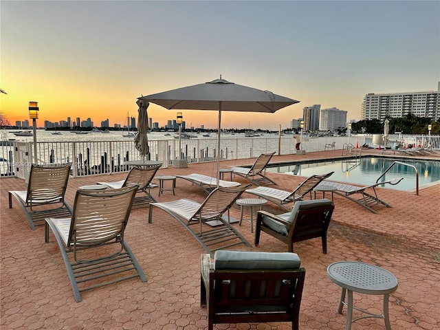 pool at dusk with a water view and a patio