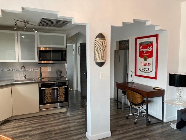 kitchen featuring stainless steel counters, dark wood-type flooring, appliances with stainless steel finishes, backsplash, and sink