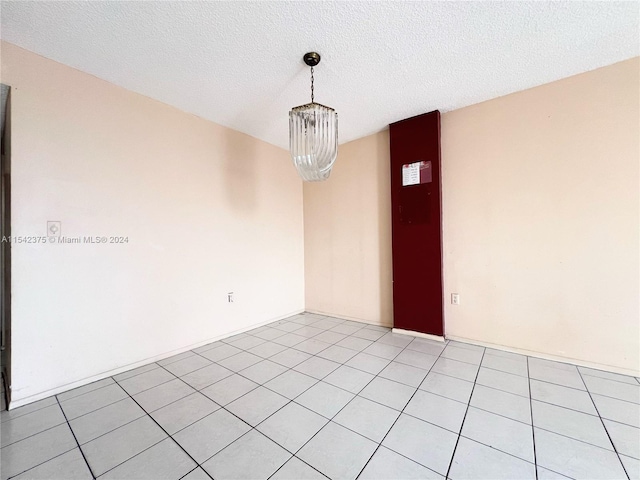 tiled spare room featuring a notable chandelier and a textured ceiling