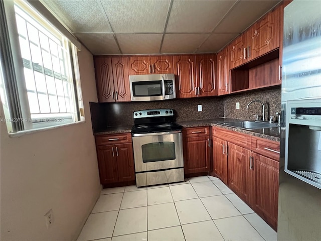 kitchen with sink, light tile floors, a paneled ceiling, backsplash, and stainless steel appliances